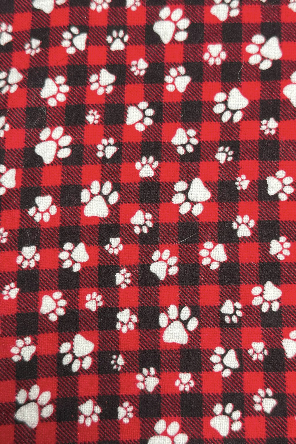 Red and black buffalo plaid fabric patterned with scattered white paw prints of various sizes.