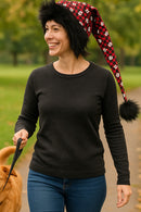 Adult walking a dog in the park wearing a handmade red plaid hat with white paw prints, black fuzzy trim, and a long drooping tail with black pom-pom.