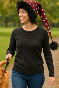 Adult walking a dog in the park wearing a handmade red plaid hat with white paw prints, black fuzzy trim, and a long drooping tail with black pom-pom.