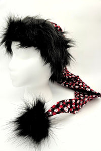 A mannequin head wearing a novelty Santa-style hat with shaggy black faux fur on top, a long red plaid fabric tail decorated with white paw prints, and a large black furry pom-pom at the end.
