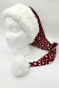 Red plaid Santa-style hat with white paw print pattern, featuring a fluffy white faux fur brim and large white pom-pom, displayed on a white mannequin head.