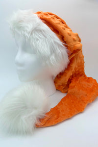 A mannequin head displays a festive(Santa-style)  hat made of textured orange fabric with raised bumps, trimmed with fluffy white faux fur around the brim and ending in a large, soft white pom-pom.