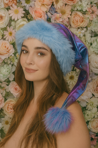 Adult wearing a handmade shimmering pastel tie-dye hat with blue trim and purple-blue pom-pom in a cozy indoor setting.