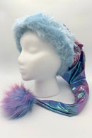 Shimmering pastel tie-dye Santa hat with a metallic blue-purple fabric body, trimmed with fluffy light blue faux fur and finished with a large fuzzy blue-and-pink pom-pom, displayed on a white mannequin head.