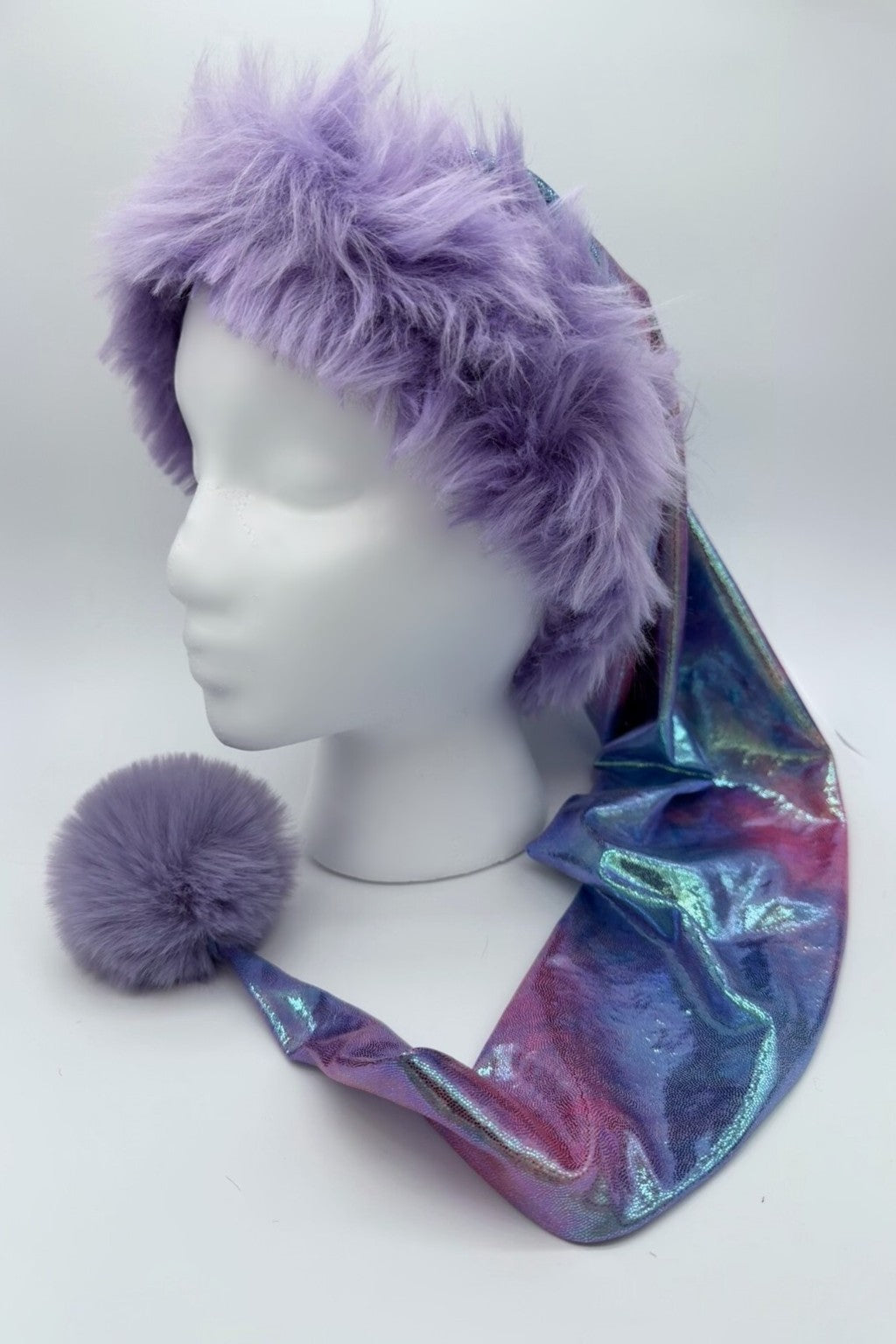 Mannequin head wearing a whimsical hat with a fluffy lavender faux fur trim and a long, shimmering pastel tie-dye fabric tail, finished with a matching lavender pom-pom at the end.
