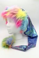 Colorful fur trimmed Santa-style hat with rainbow faux fur in pink, yellow, blue, and green, featuring a long metallic iridescent tail ending in a fluffy rsainbow colored pom-pom, displayed on a white mannequin head.