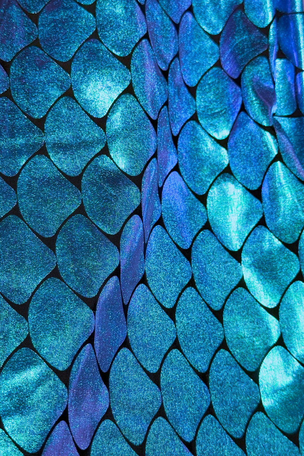 Close-up of shiny, iridescent fabric patterned with overlapping Teal and blue scales resembling mermaid or fish scales.