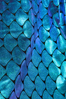 Close-up of shiny, iridescent fabric patterned with overlapping Teal and blue scales resembling mermaid or fish scales.