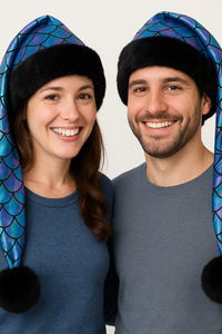 Two adults wearing handmade shimmering mermaid scale hats with black faux-fur trim and black pom, playful and stylish.