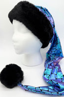 A mannequin head wearing a long, pointed hat with a wide black faux-fur brim and a shiny, iridescent fabric in blue and purple with a scale-like pattern. The hat extends down to the side, ending in a large black faux-fur pompom.