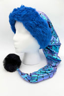 Mannequin head wearing a festive hat with a wide, fluffy blue faux-fur brim, a long metallic purple and Teal mermaid-scale patterned tail, and a large black pom-pom at the tip.