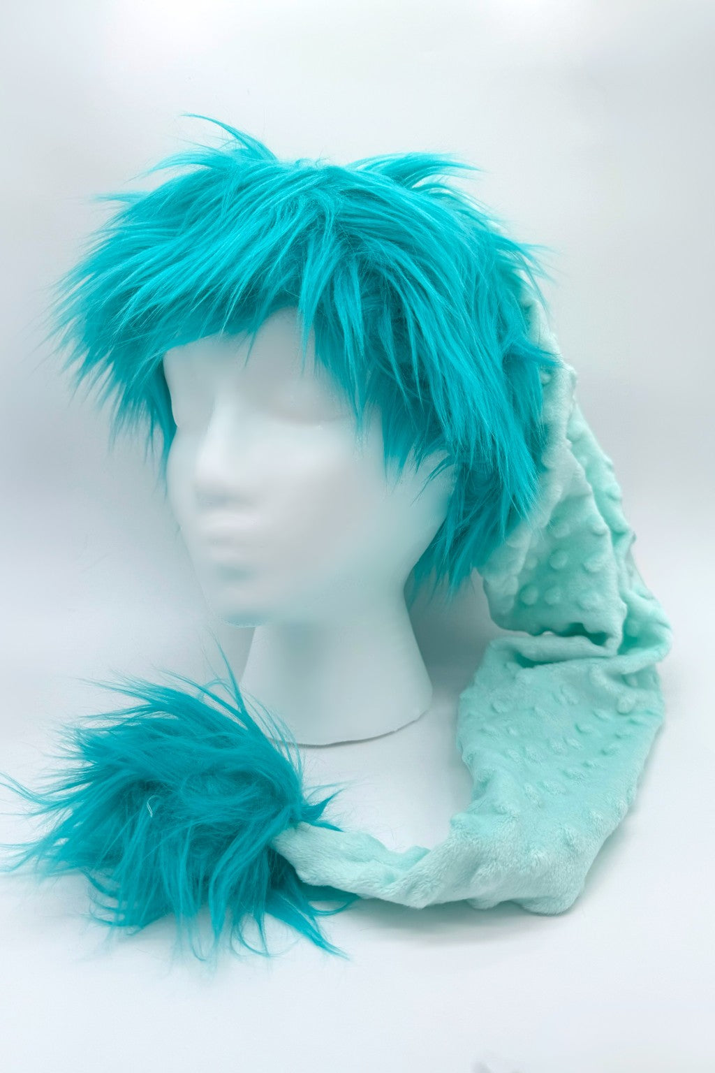 A mannequin head with a short, spiky Teal trimmed Santa-style hat, soft textured tail-like extension ending in a fluffy Teal pom-pom, displayed against a white backdrop.