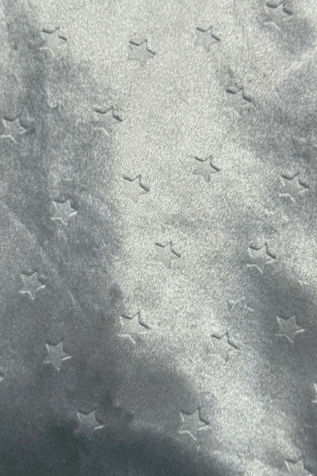 Close-up of a soft, light silvery gray fabric with a subtle embossed star pattern.