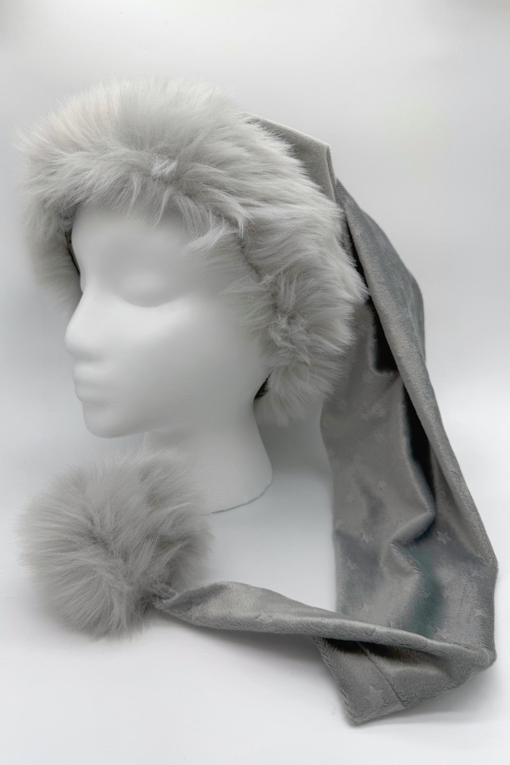 A silver Velvet  with a subtle embossed star patternSanta-style hat with fluffy gray faux fur trim and a large matching pom-pom, displayed on a white mannequin head.
