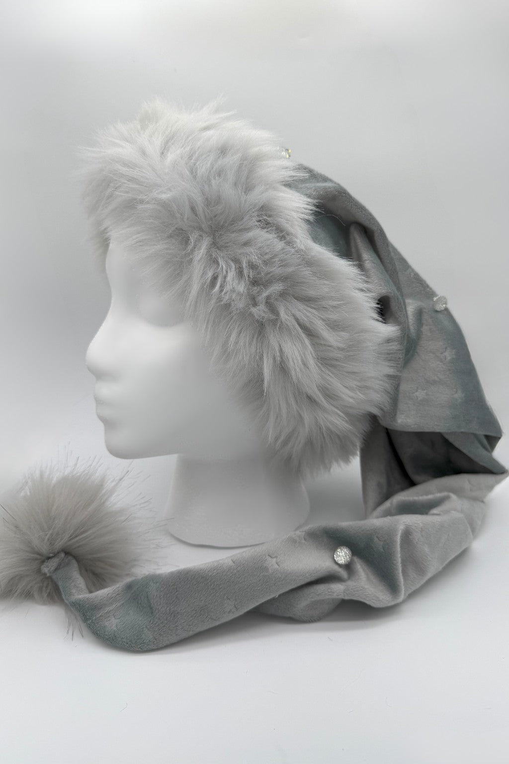 Gray faux fur trimmed Santa-style hat of a silvery gray Velvet with embosssed stars, jeweled accents, and a fluffy matching pom-pom, displayed on a white mannequin head.