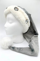 Gray Velvet Santa-style hat of silvery gray Velvet with embossed stars has a white faux fur trim and large rhinestone embellishments, and other more ssubtle jewel accents is finished with a fluffy white pom-pom at the tip, displayed on a white mannequin head.