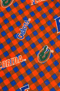 Orange and blue plaid fabric patterned with University of Florida Gators logos, including the word “Florida,” the script “Gators,” a large blue “F,” and the green alligator head mascot.