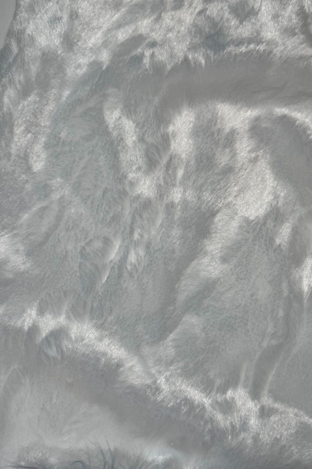 Close-up of a soft, shiny white faux fur fabric with a silky texture and light reflecting off its surface.”