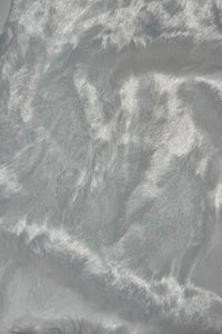 Close-up of a soft, shiny white faux fur fabric with a silky texture and light reflecting off its surface.”