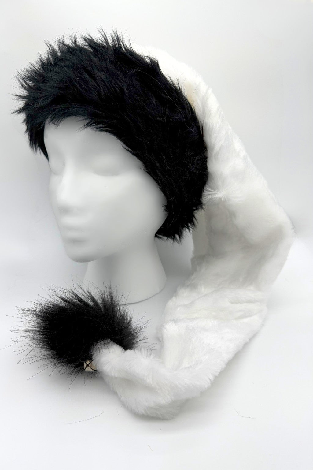 A white faux fur Santa-style hat with a black faux fur trim and a black fluffy pom-pom at the tip, displayed on a white mannequin head against a plain background.