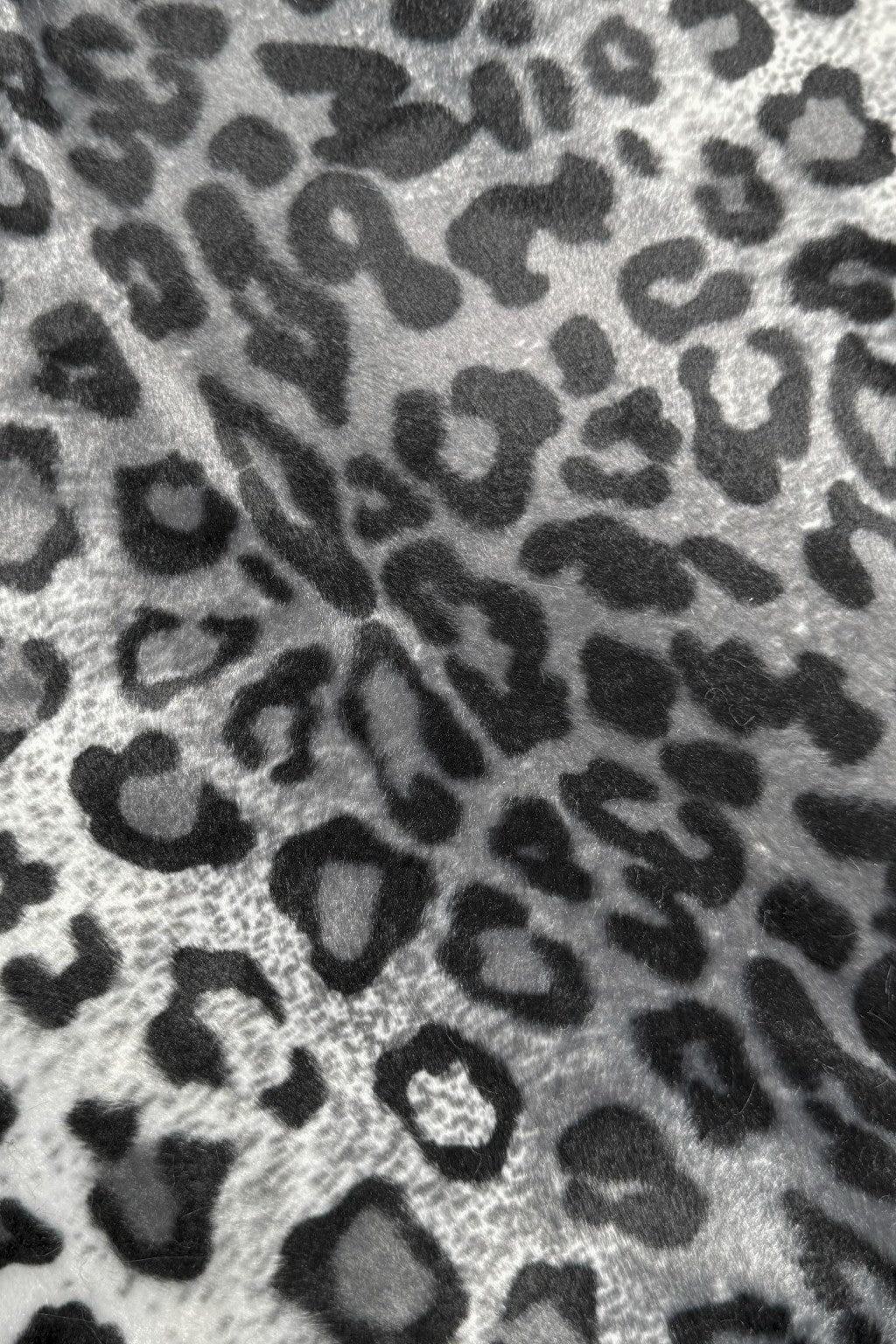 Close-up of a gray and black leopard print fabric with irregular dark spots and rosettes on a lighter background.