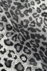 Close-up of a gray and black leopard print fabric with irregular dark spots and rosettes on a lighter background.