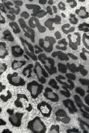 Close-up of a gray and black leopard print fabric with irregular dark spots and rosettes on a lighter background.