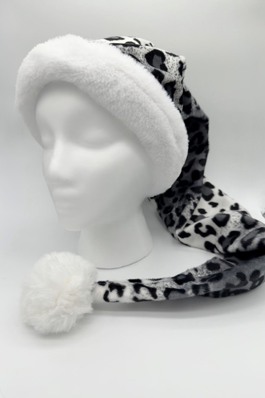 A gray and black leopard-print Santa-style hat with a fluffy white faux fur brim and a large white pom-pom at the end, displayed on a white mannequin head against a plain background.