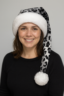 Smiling woman wearing a handmade gray leopard print hat with soft white trim and a fluffy white pom-pom, styled to droop naturally over her shoulder.