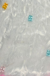 Colorful translucent teddy bear charms in yellow, blue, pink, and green scattered on a soft, white, furry fabric background.