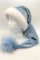 A light blue Velvet Santa-style hat with a fluffy white faux fur brim and a long tail ending in a large blue faux fur pom-pom tipped with gray. The hat is displayed on a white mannequin head against a plain background.