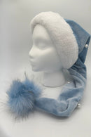 Light blue Velvet Santa-style hat with a fluffy white faux fur brim, pearl-like accents along the tail, and a large fluffy blue pom-pom tip, displayed on a white mannequin head against a neutral background.