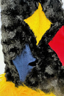A close-up of a textured fabric design featuring a black furry background with three diamond-shaped patches in bright colors—yellow, red, and blue—along with some fluffy yellow fur at the bottom.