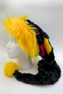 A black and yellow furry novelty (Santa-style) hat displayed on a white mannequin head. The hat features a bright yellow faux fur trim, long black plush sides that extend down, a red, blue and yellow diamond shaped insets, and a fluffy yellow pom-pom at the end of the hanging section.