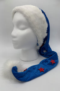 A mannequin head displays a festive Santa-style hat with a fluffy white faux fur trim and pom-pom. The main fabric of the hat is bright blue, decorated with red star-shaped buttons and white star accents. The long tail of the hat drapes down and curls forward across the mannequin’s chest.