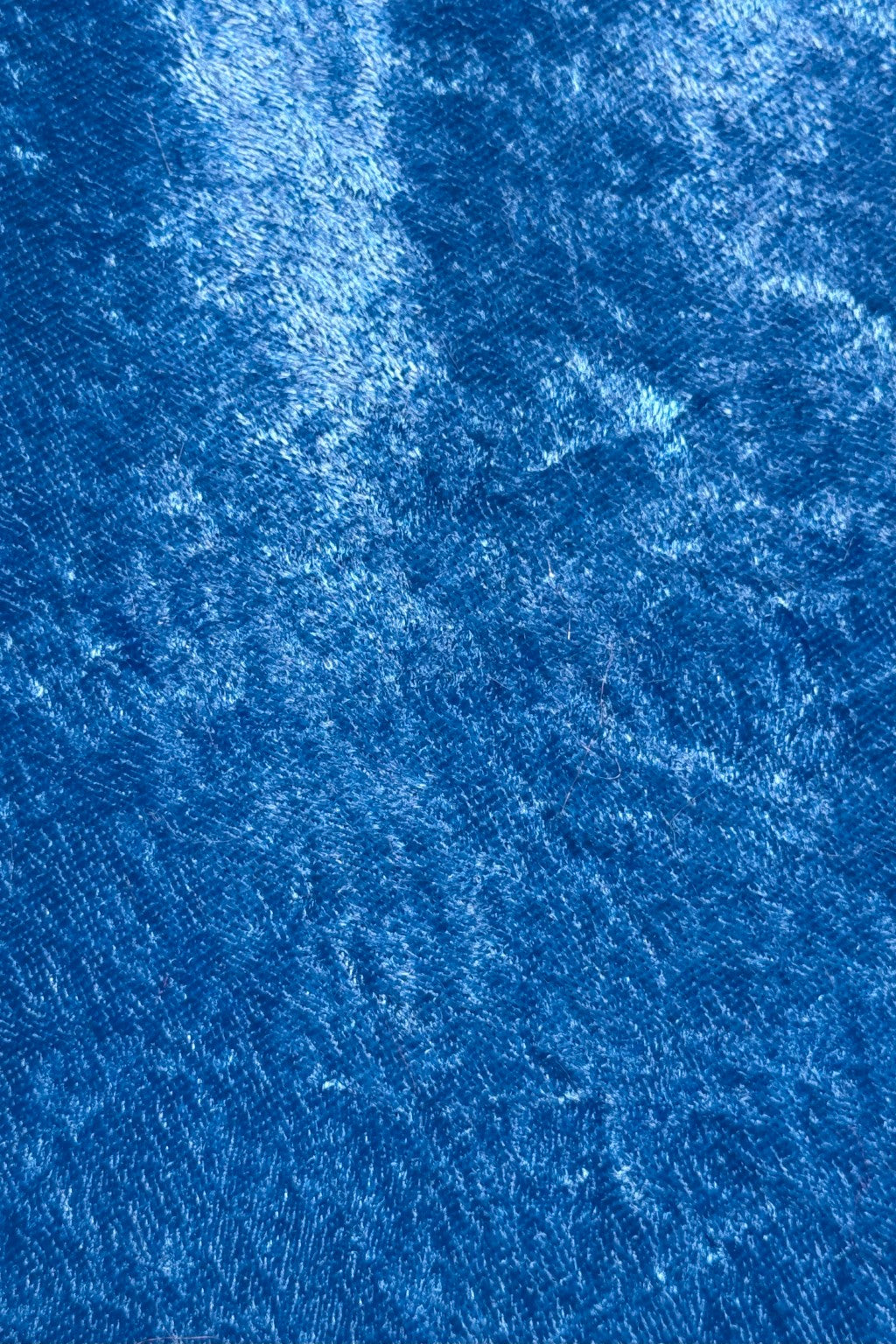 Close-up view of a blue crushed Velvet fabric, showing its soft texture, sheen, and light reflections that create a shimmering effect.