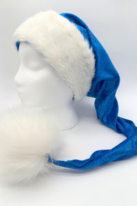 Blue Velvet Santa-style hat with a wide white faux fur trim and an oversized fluffy white pom-pom at the end, displayed on a white mannequin head.