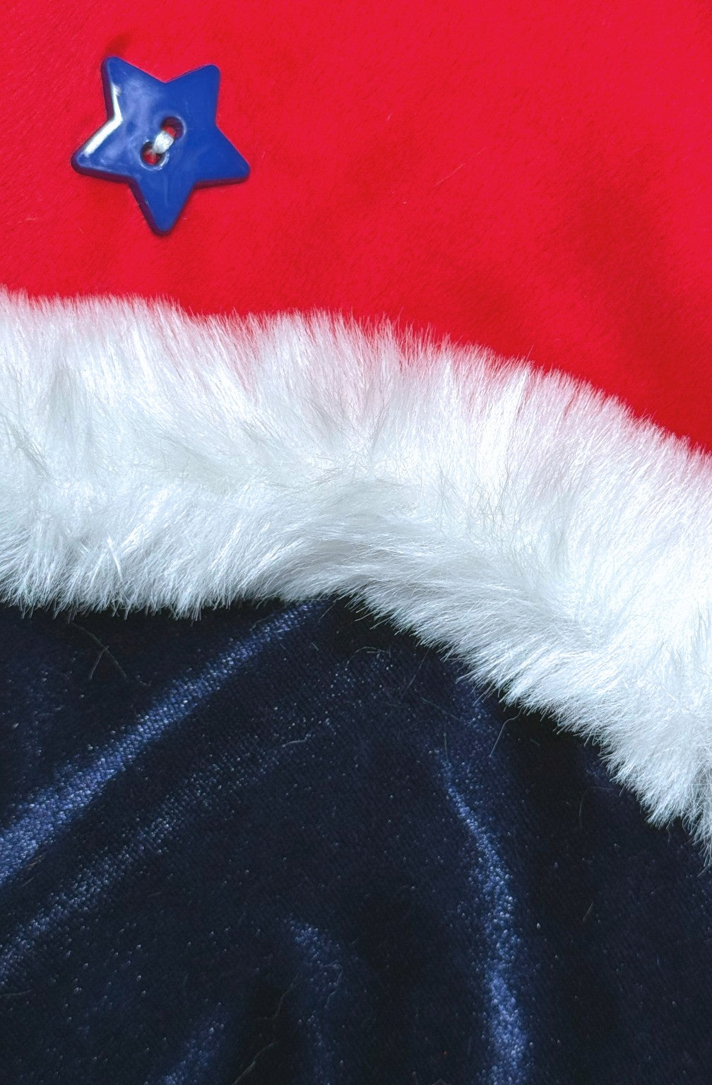 Close-up of a fabric design showing three sections: a red felt-like material at the top with a shiny blue star-shaped button, a white faux fur trim running horizontally across the middle, and a dark blue Velvet-like fabric at the bottom