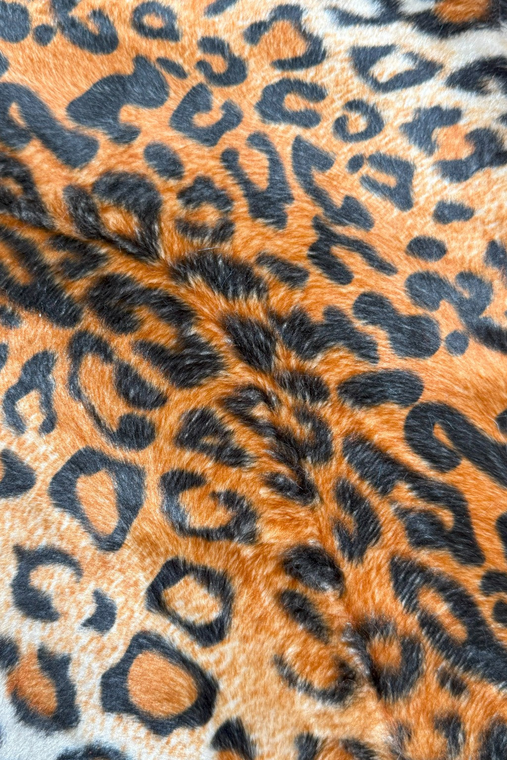 Close-up view of orange and black leopard print faux fur fabric, showing soft texture and bold spotted pattern.