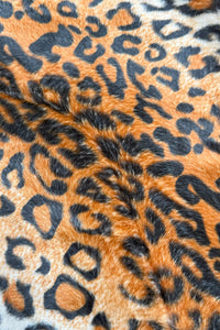 Close-up view of orange and black leopard print faux fur fabric, showing soft texture and bold spotted pattern.