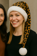 An adult model standing near a friend wearing a brown leopard print hat with white trim and white pom-pom.