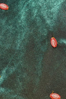 Small red footpom-pom-shaped buttons with white laces printed on them scattered across a dark green, Velvet fabric background.