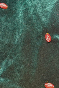 Small red footpom-pom-shaped buttons with white laces printed on them scattered across a dark green, Velvet fabric background.