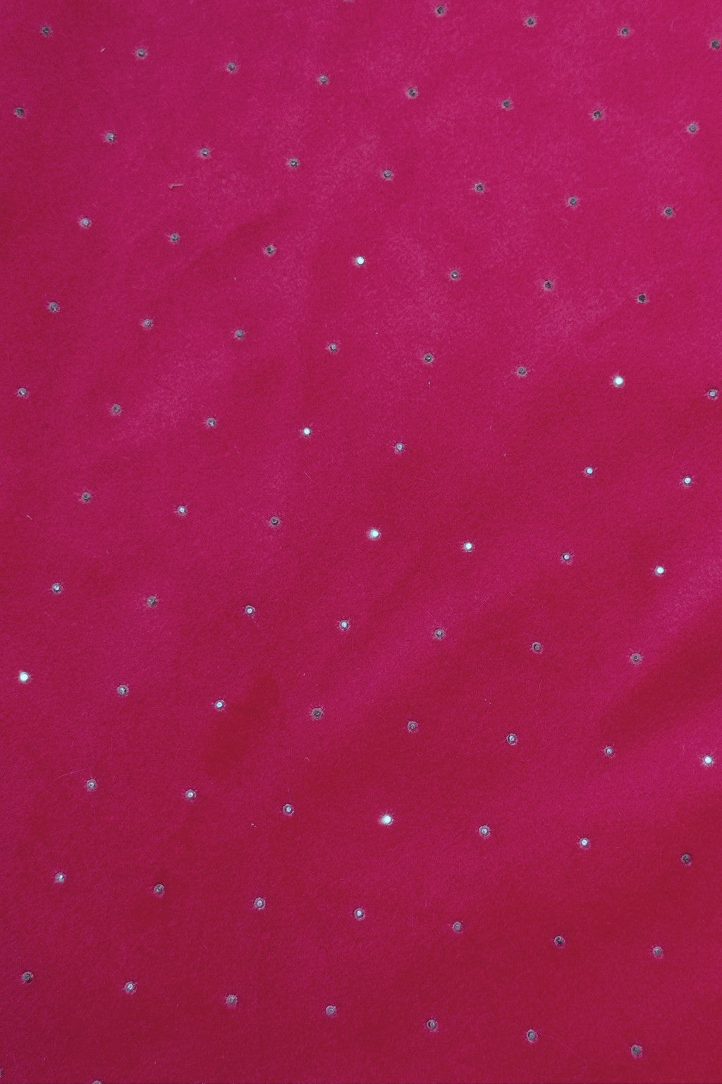 A close-up of a bright pink fabric with small, evenly spaced silver rhinestones scattered across the surface, creating a sparkling effect.