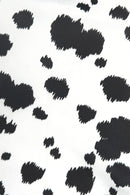 Close-up of a white fabric with an irregular black cow print pattern, featuring scattered black spots of varying sizes across the surface.