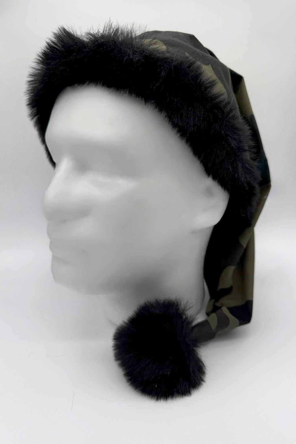 Camouflage Santa-style hat with black faux fur trim and a matching black pom-pom, displayed on a white mannequin head.