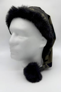 Camouflage Santa-style hat with black faux fur trim and a matching black pom-pom, displayed on a white mannequin head.