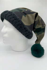 Camouflage Santa-style hat with black faux fur trim and a large forrest green fluffy pom-pom, displayed on a white mannequin head against a plain background.