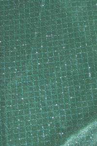 Close-up of a mossy green fabric with a subtle grid pattern and shimmering glitter highlights, reflecting light across the surface.