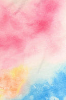 Close-up of a pastel tie-dye fabric featuring soft blends of pink, blue, yellow, and orange hues. The colors fade into each other, creating a dreamy watercolor effect on the textured cloth.